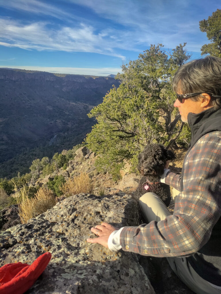 Dr. Clifford Scott sitting with his black poodle dog on the edge of the Rio Grande Gorge.