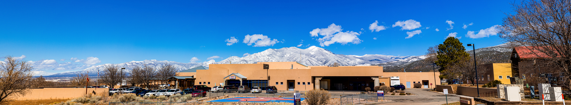 Brown stuccoed building that looks like a hospital with a mountain behind it.