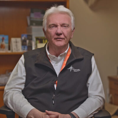 A man in a black vest sits in an office, discussing topics related to Holy Cross Medical Center.