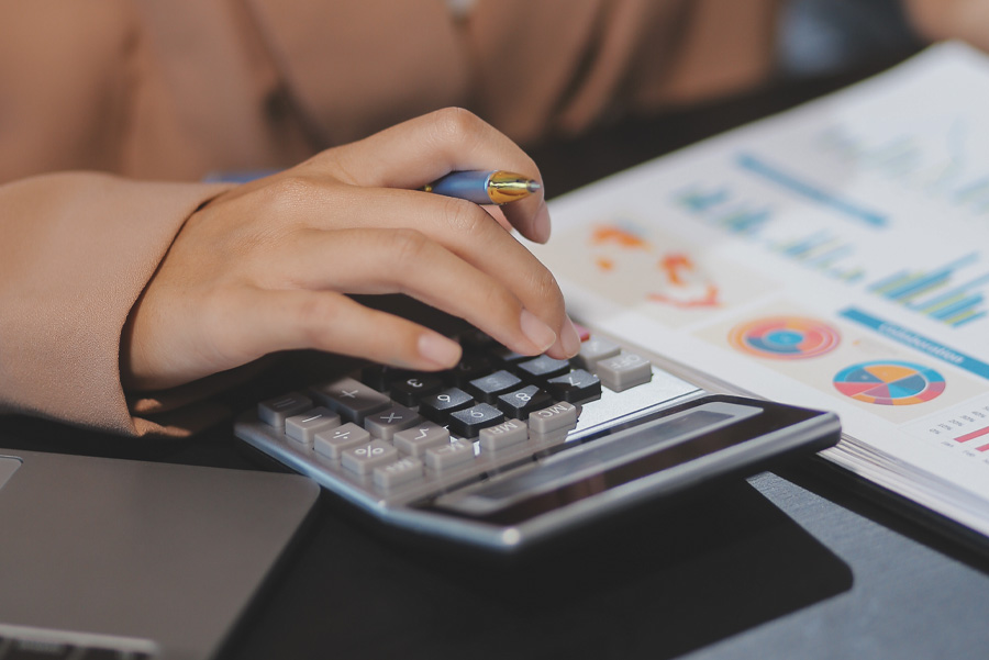 A hand using a calculator with financial reports and graphs visible on the table, highlighting data analysis.