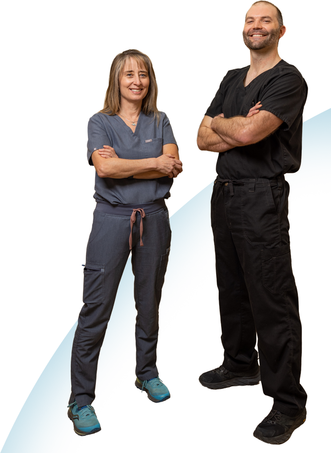 Two healthcare professionals, one female and one male, stand confidently with arms crossed, wearing scrubs and smiling.